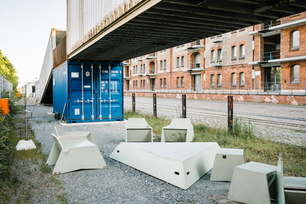 Weiße Betonmöbel vor blauem Schiffscontainer, Backsteingebäude des Speicher XI dahinter.