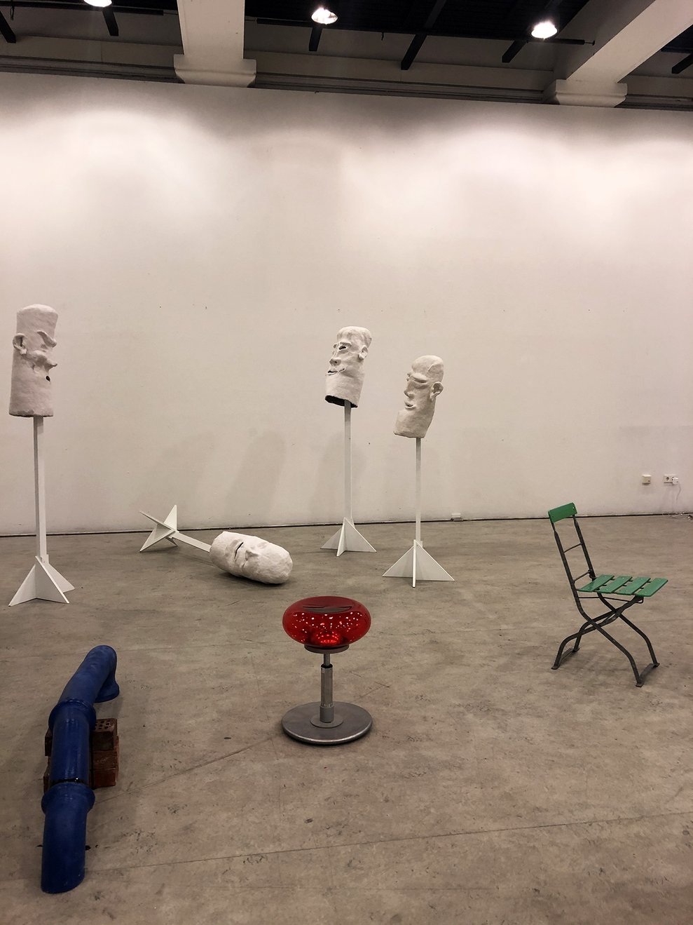 Installation von Laura Pientka mit weißen Kopfskulpturen auf Ständern, Stühlen und blauen Rohren.