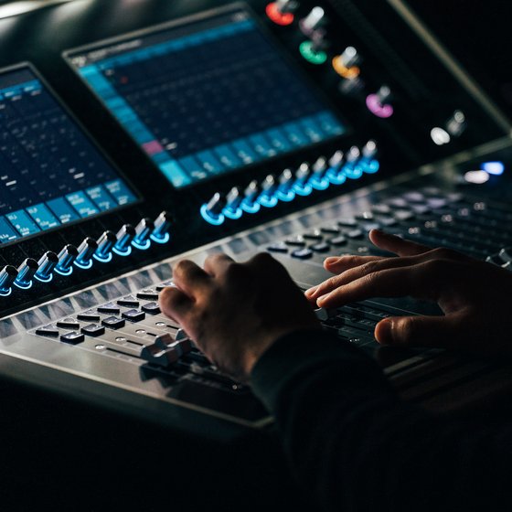 Hände bedienen ein Soundmischpult mit beleuchteten Reglern und digitalen Anzeigen, im Fokus auf Audioanpassung und -produktion