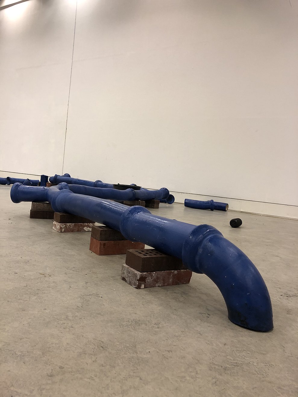 Blaue Keramikrohr-Skulpturen auf Ziegeln im Galerieraum von Laura Pientka.