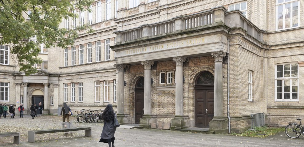 Historic building at Dechanatstraße housing the Faculty of Music, University of the Arts Bremen, featuring classical architecture with columns and large windows. Students are gathered outside, and bicycles are parked nearby.