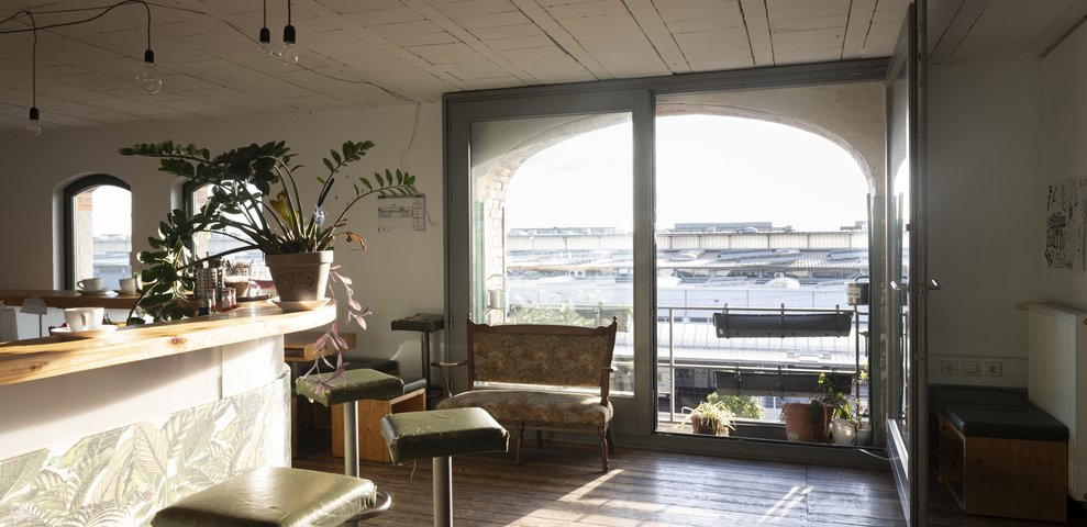 Sunlight floods the room of Café Lu at HfK Bremen, plants and furniture in the foreground.