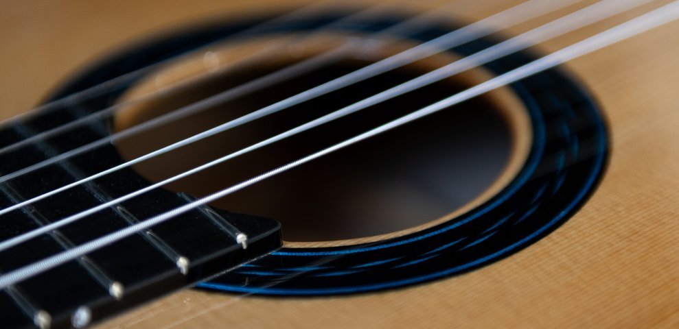 Nahaufnahme des Schalllochs einer klassischen Gitarre mit Nylon- und umsponnenen Saiten und blauer Rosette.