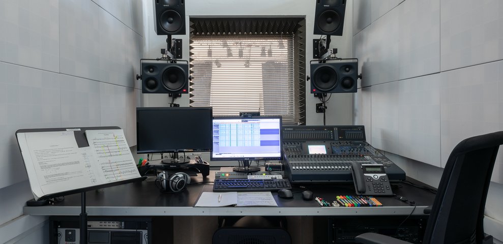Recording Studio at HfK Bremen featuring mixing console, dual monitors, headphones, and wall-mounted speakers.