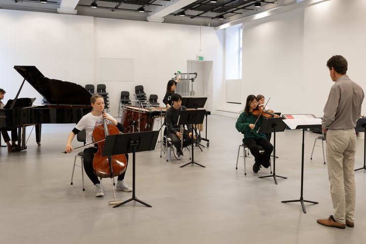 Ensemble rehearsing new music with grand piano and strings in a hall.