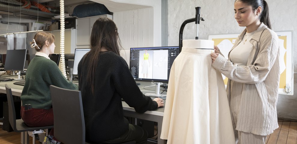 Studierende arbeiten im Mode-CAD-Studio der HfK Bremen und nutzen Computer sowie eine Schneiderpuppe für die Gestaltung von Kleidung.
