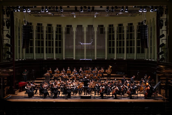 Das Sinfonieorchester der HfK Bremen spielt mit Dirigentin auf einer Konzertbühne vor großer Orgel.