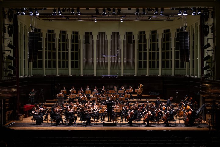 Das Sinfonieorchester der HfK Bremen spielt mit Dirigentin auf einer Konzertbühne vor großer Orgel.
