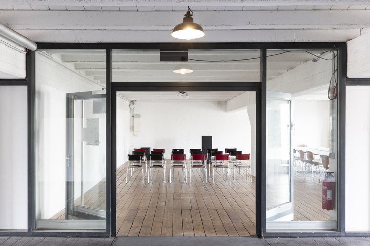 Konferenzraum mit Stühlen, Holzboden und großen Glasfenstern.