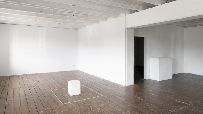 Galerie Flut. Lichtdurchfluteter Raum mit Holzboden, weißen Wänden und einem kleinen, weißen Würfel in der Mitte.