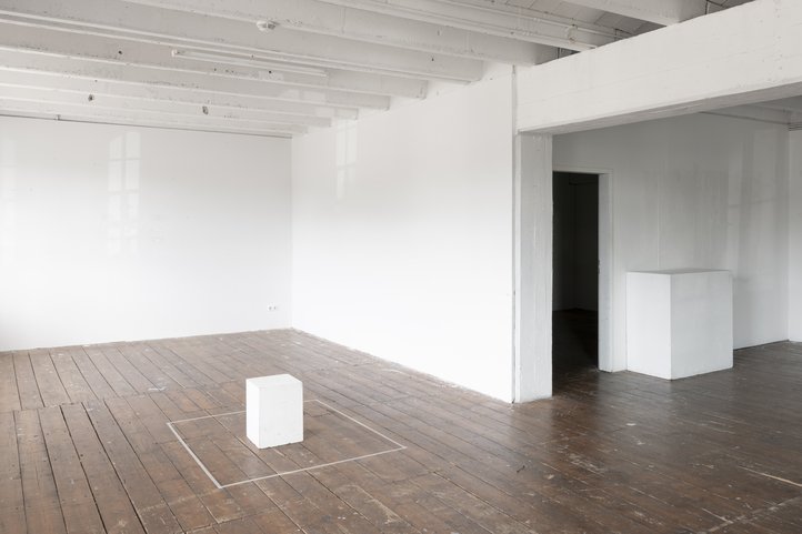 Galerie Flut. Light-filled room with wooden floor, white walls, and a small white cube in the centre.