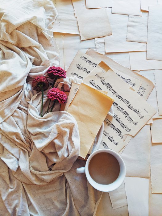 Sheet music, a cup of white coffee and red flowers on pale fabric.