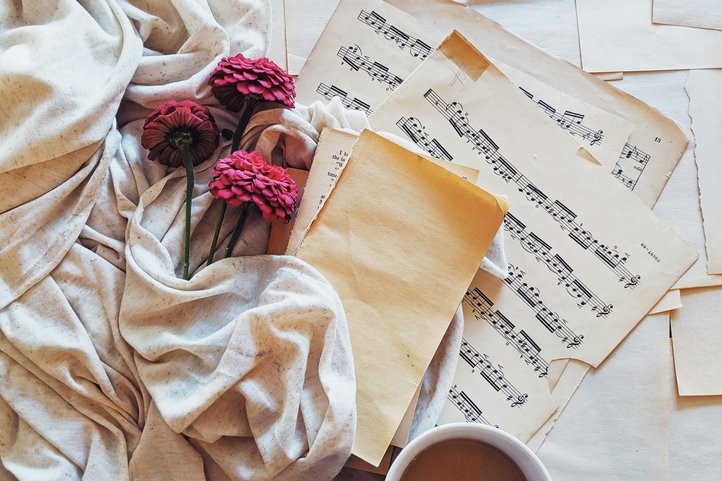 Notenblätter, eine Tasse Milchkaffee und rote Blumen auf hellem Stoff.