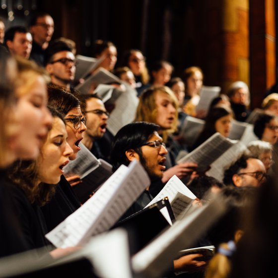 Ein Chor singt gemeinsam, hält Notenblätter in einer schummrig beleuchteten Kirche.