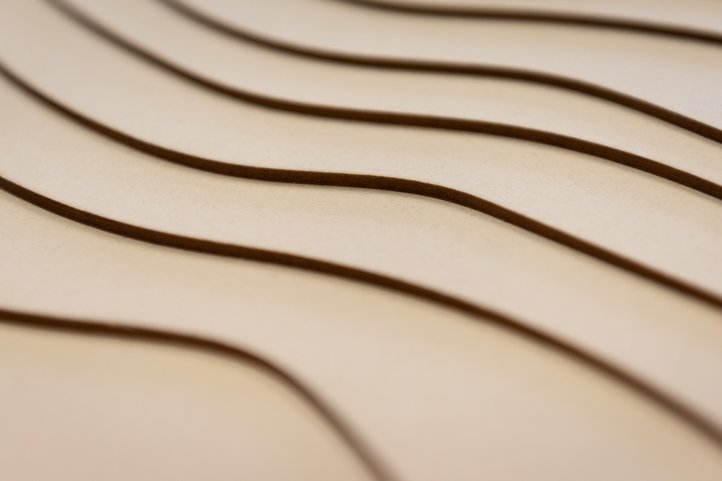 Nahaufnahme einer lasergeschnittenen Holzoberfläche mit geschwungenen Rillen.