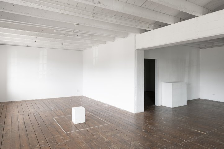 Galerie Flut. Lichtdurchfluteter Raum mit Holzboden, weißen Wänden und einem kleinen, weißen Würfel in der Mitte.