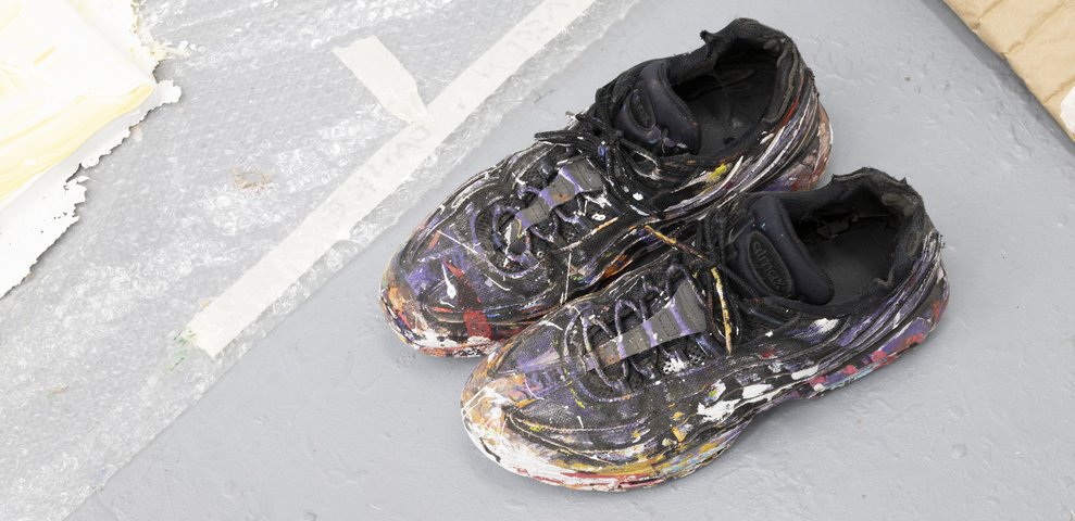 Mit Farbe bedeckte Schuhe auf dem Atelierboden als Zeichen intensiver Malarbeit.