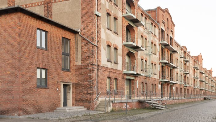 Historic brick facade of Speicher XI at HfK Bremen, showcasing its industrial architectural design and multiple balconies along a cobblestone pathway.