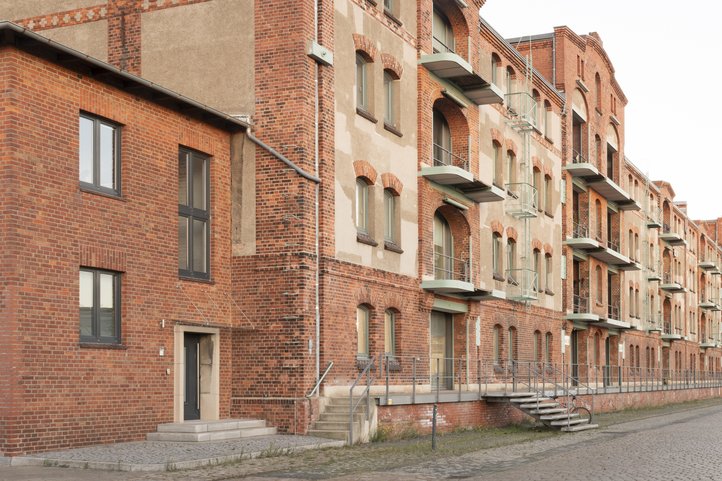 Historic brick facade of Speicher XI at HfK Bremen, showcasing its industrial architectural design and multiple balconies along a cobblestone pathway.