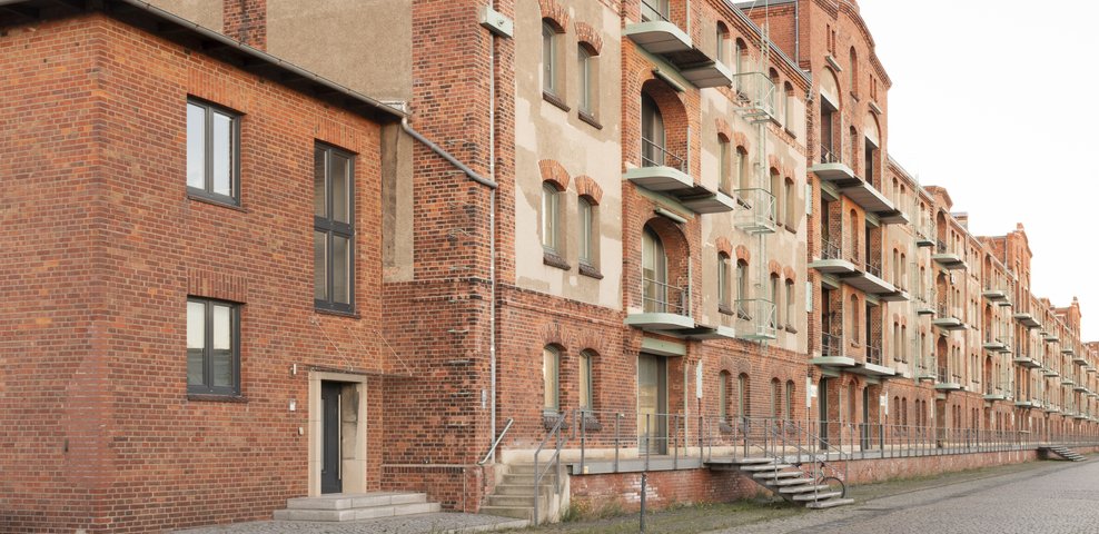 Historische Ziegelfassade des Speicher XI der HfK Bremen, die das industrielle architektonische Design und die zahlreichen Balkone entlang eines Kopfsteinpflasterwegs zeigt.