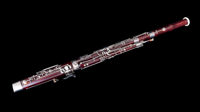 Maple wood bassoon with silver keys against black background.