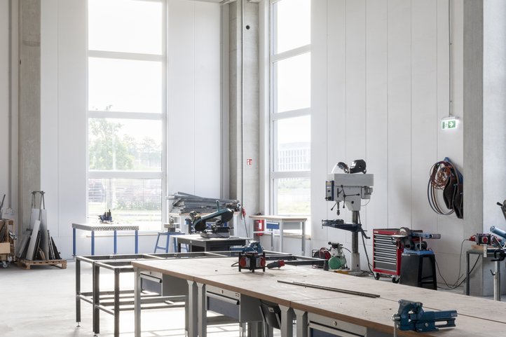 Innenraum eines Arbeitsbereichs im Speicher XI A der Hochschule für Künste Bremen mit großen Fenstern, Arbeitstischen und industriellen Geräten.