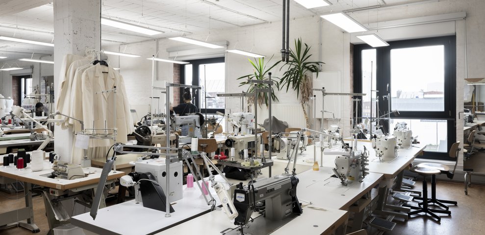 HfK Bremen Fashion Workshop featuring sewing machines, mannequins, and garments, illuminated by natural light from large windows.