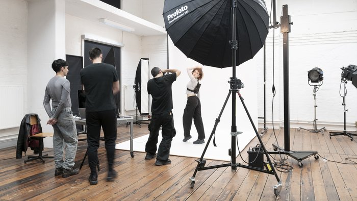 Fotostudiosession an der Hochschule für Künste Bremen: Eine Person posiert unter professioneller Beleuchtung, während Fotograf:innen und Assistent:innen aktiv eingebunden sind.