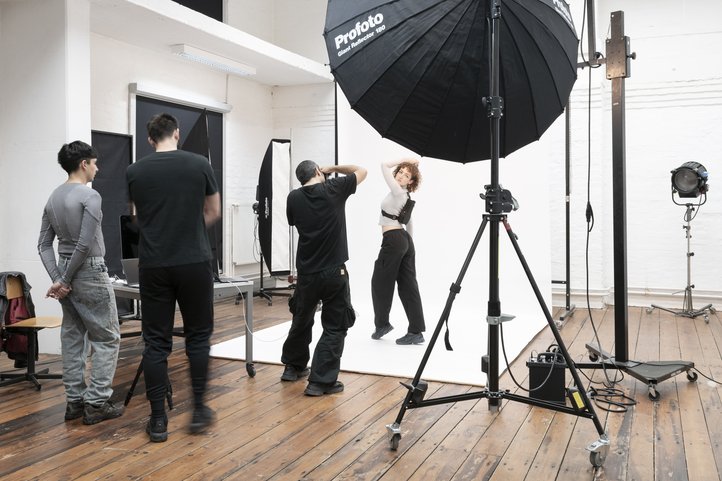 Fotostudiosession an der Hochschule für Künste Bremen: Eine Person posiert unter professioneller Beleuchtung, während Fotograf:innen und Assistent:innen aktiv eingebunden sind.