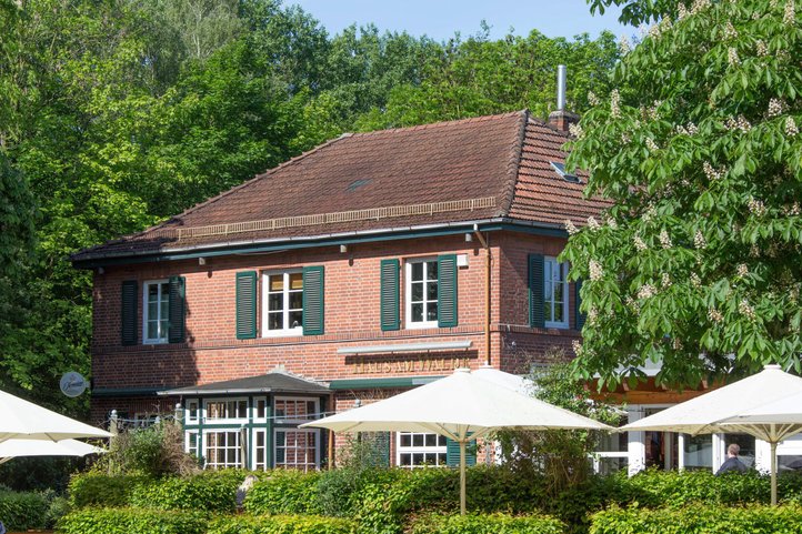 Haus am Walde in Bremen, charmantes rotes Backsteingebäude mit grünen Fensterläden, umgeben von üppigen Bäumen und Außenbestuhlung