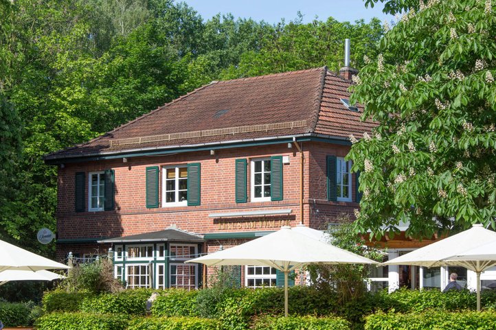 Haus am Walde in Bremen, charming red brick building with green shutters, surrounded by lush trees and outdoor seating